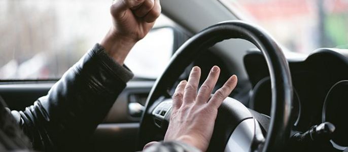 Die Hände einer Person auf dem Lenkrad eines Autos, wobei eine Hand zur Faust geballt ist und die andere auf dem Lenkrad liegt.