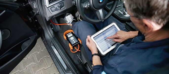 Ein Mann in einem Auto, der ein Tablet benutzt, um etwas auf dem Armaturenbrett des Autos zu überprüfen.