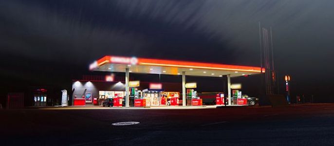 Eine gut beleuchtete Tankstelle bei Nacht, mit einem auffälligen roten Vordach und mehreren Zapfsäulen.