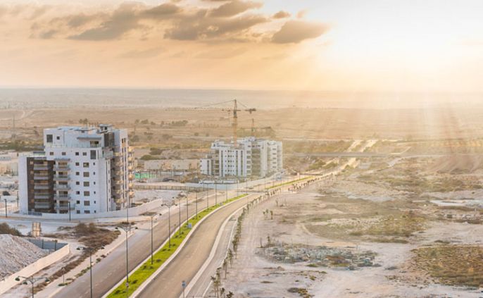 Eine moderne Stadtlandschaft bei Sonnenuntergang, mit mehreren im Bau befindlichen Gebäuden, einer kurvenreichen Straße und einer weiten Landschaft im Hintergrund.