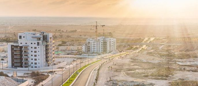 Eine moderne Stadtlandschaft bei Sonnenuntergang, mit mehreren im Bau befindlichen Gebäuden, einer kurvenreichen Straße und einer weiten Landschaft im Hintergrund.