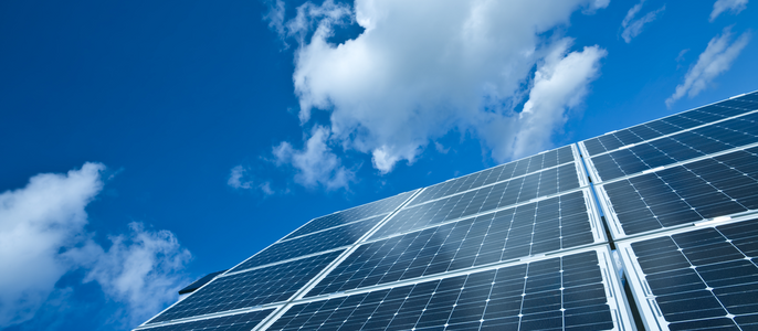 Eine Reihe von Sonnenkollektoren vor einem klaren blauen Himmel mit vereinzelten weißen Wolken.