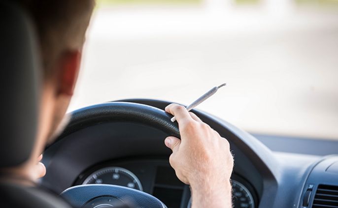 Eine Person, die ein Auto fährt und einen Joint auf dem Lenkrad hält.