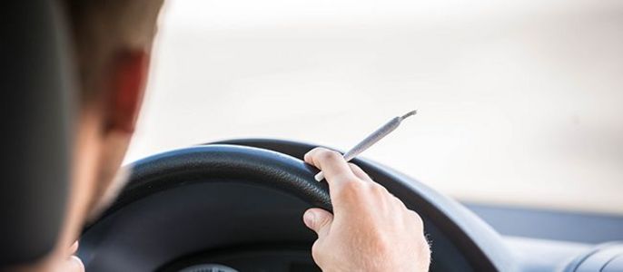 Eine Person, die ein Auto fährt und einen Joint auf dem Lenkrad hält.