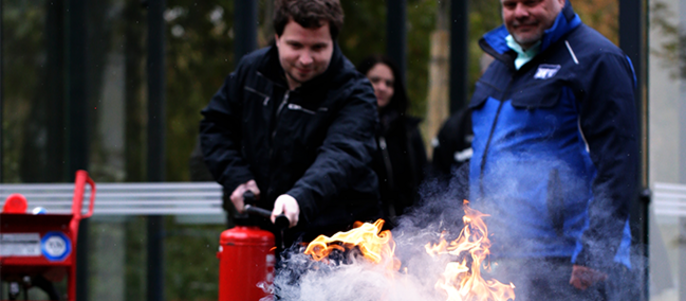 Zwei Männer, von denen einer einen roten Feuerlöscher benutzt, um ein kleines Feuer zu löschen.