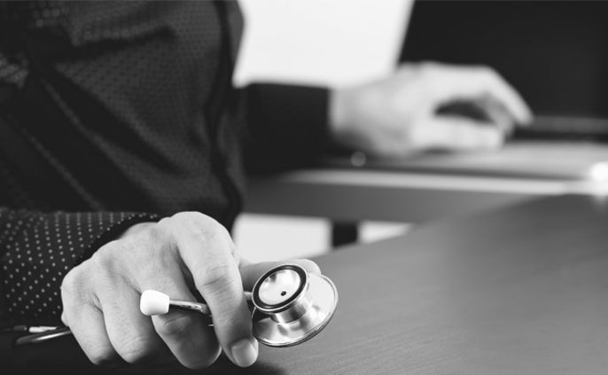 Die Hand einer Person hält ein Stethoskop, während sie auf einem Laptop tippt.