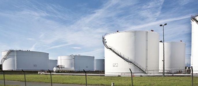 Eine große Industrieanlage mit mehreren weißen zylindrischen Tanks unter einem klaren blauen Himmel mit vereinzelten Wolken.