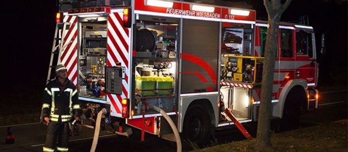 Ein Feuerwehrauto mit geöffnetem Kofferraum, in dem verschiedene Ausrüstungsgegenstände zu sehen sind, und ein Feuerwehrmann, der daneben steht.