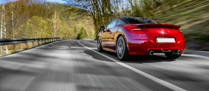 Ein roter Sportwagen, der eine von Bäumen gesäumte Straße hinunterfährt, mit einem unscharfen Hintergrund, der die Essenz von Bewegung und Natur einfängt.