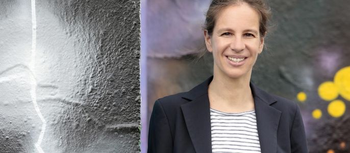 Eine Frau mit fröhlichem Gesichtsausdruck, die vor dem Hintergrund einer strukturierten Wand mit einer Mischung aus Farben steht.